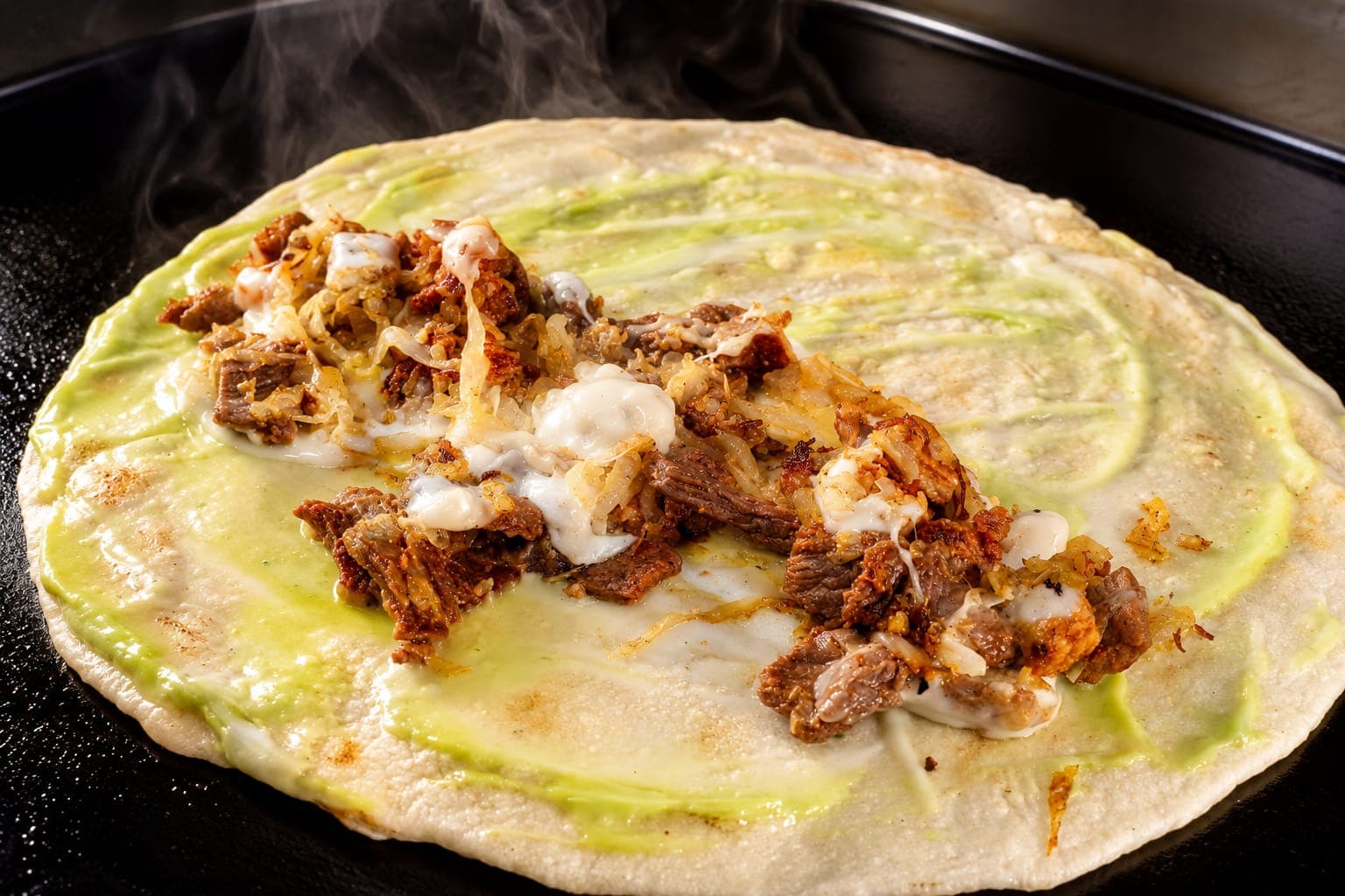 Tortilla de harina abierta en la plancha, con aguacate, carne en trocitos y queso derretido