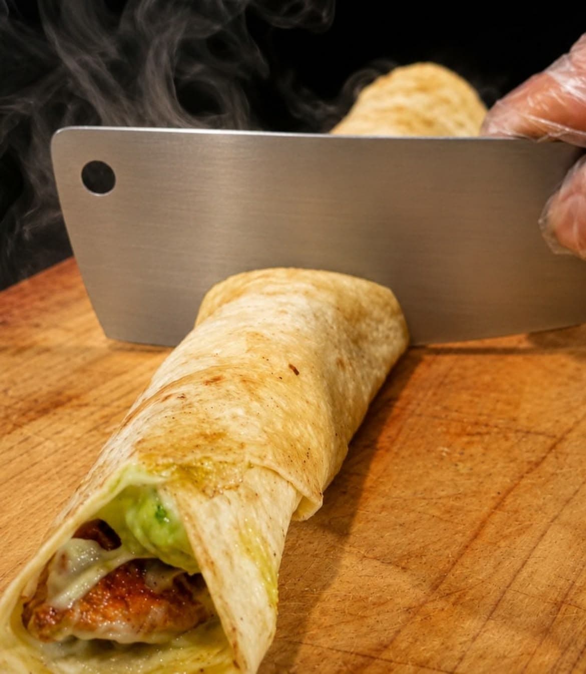 Tortilla de harina enrollada siendo cortada con machete sobre una tabla de madera, con el relleno a la vista